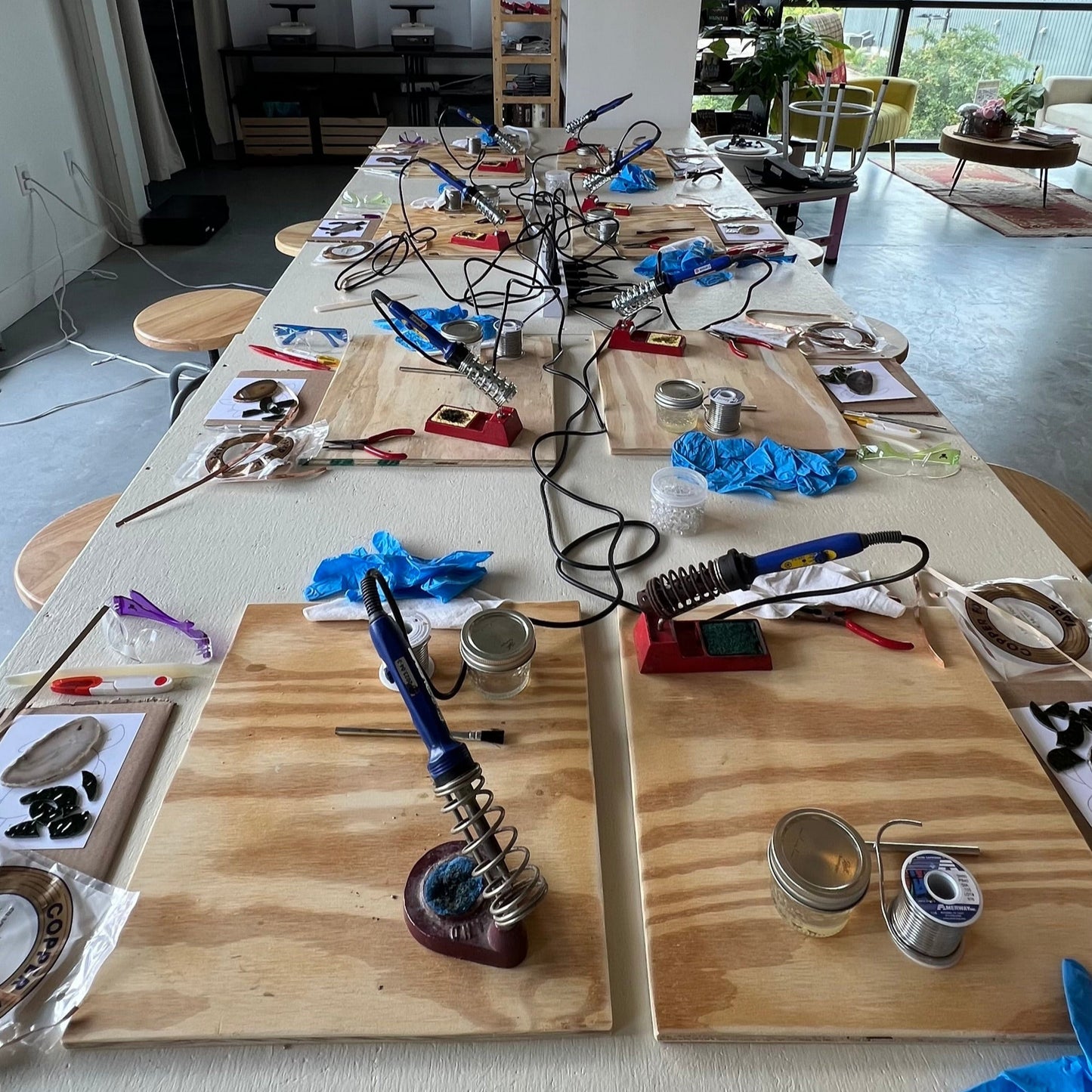 Workshop area with tools and materials on a large table, surrounded by chairs.