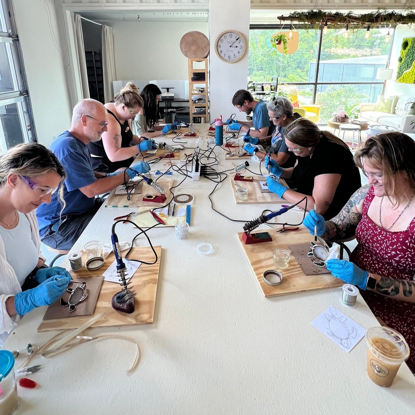 Group of people working on a craft project in a bright room with large windows.